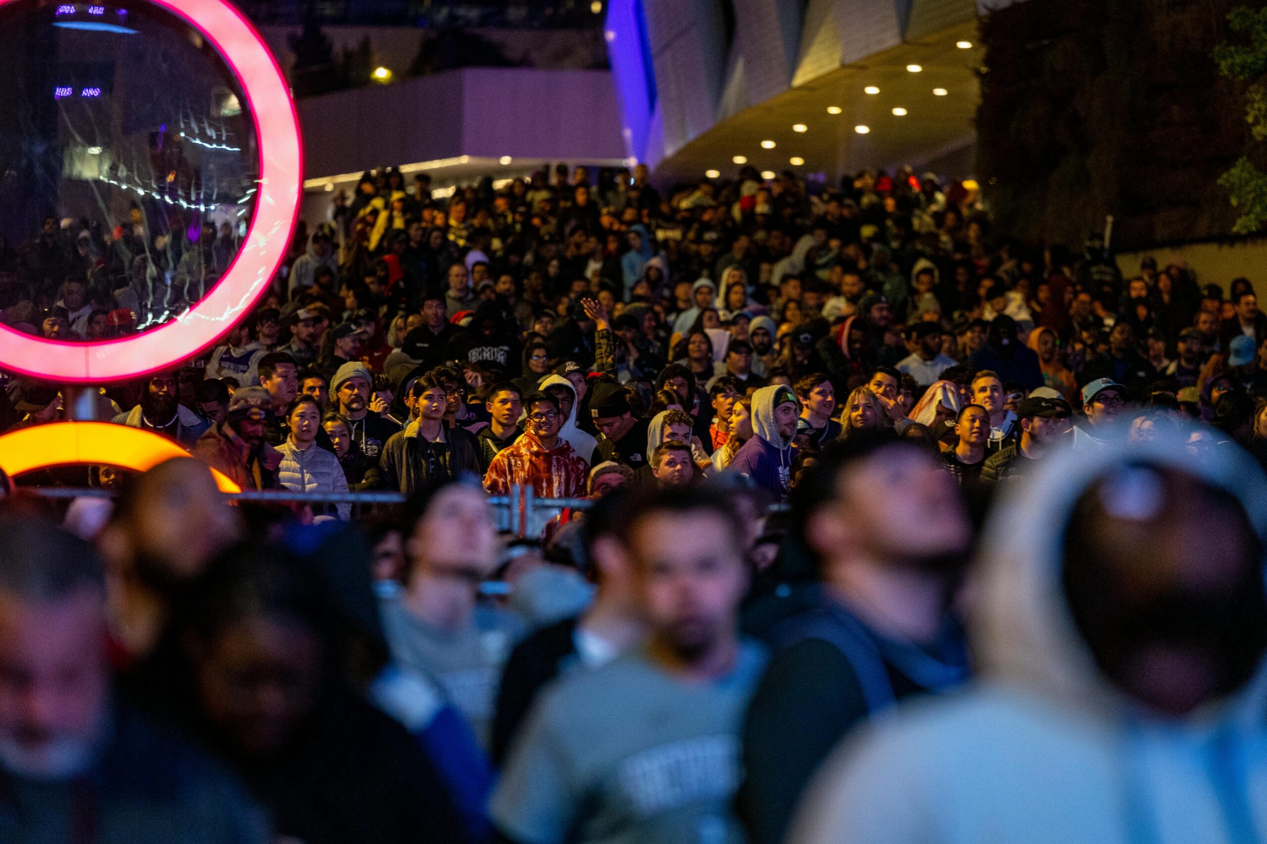 A lively crowd gathered outdoors at night under colorful lights.
